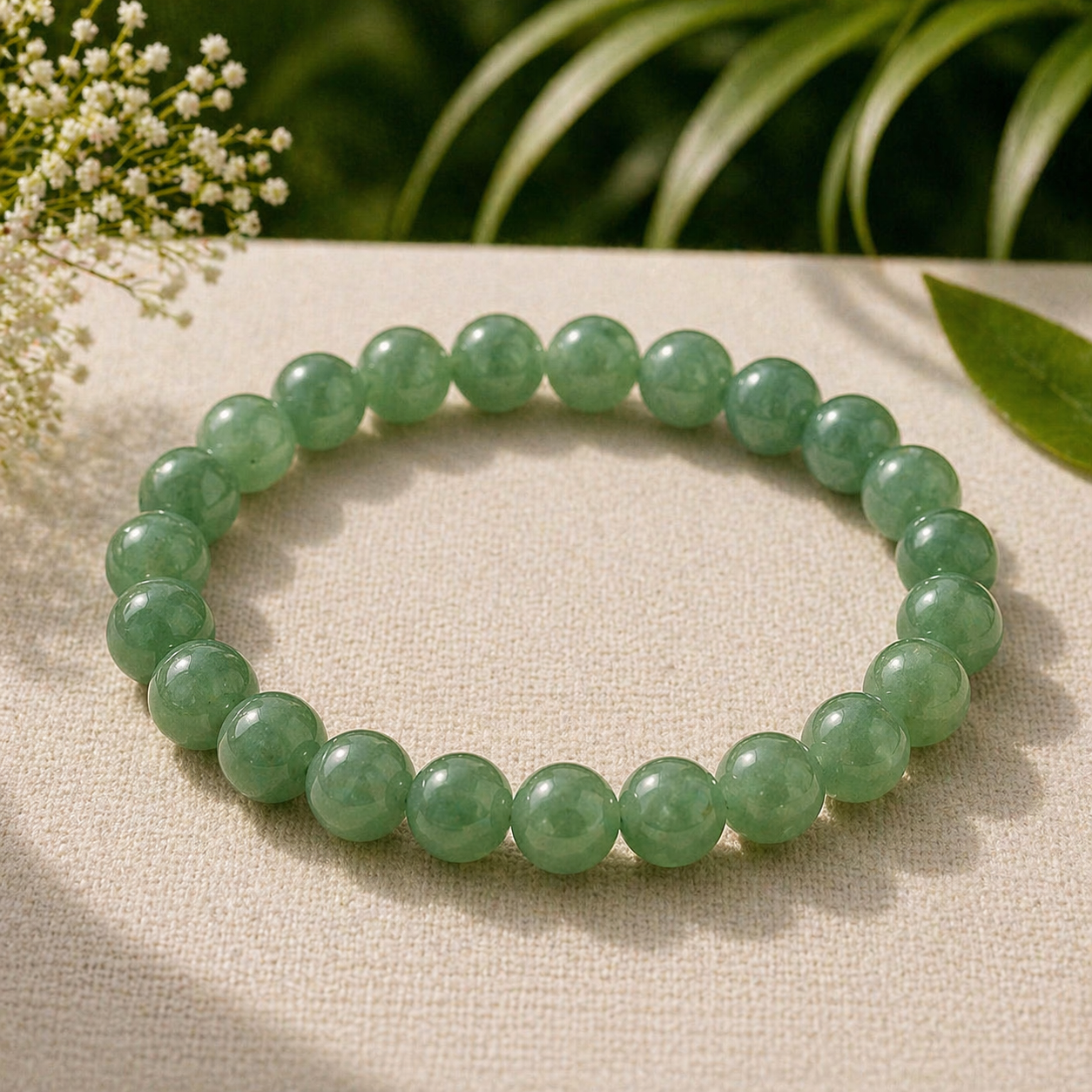 Green aventurine bracelet on a beige fabric background with green leaves and white flowers.